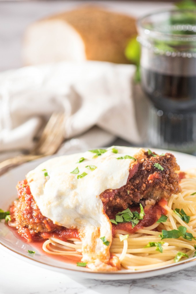 Authentic Chicken Parmesan on white plate with glass of wine 