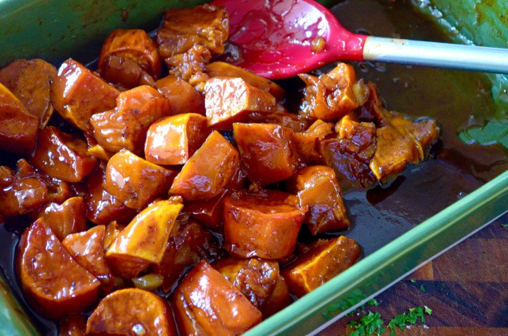 Candied sweet potatoes in a green dish with a red serving spoon 