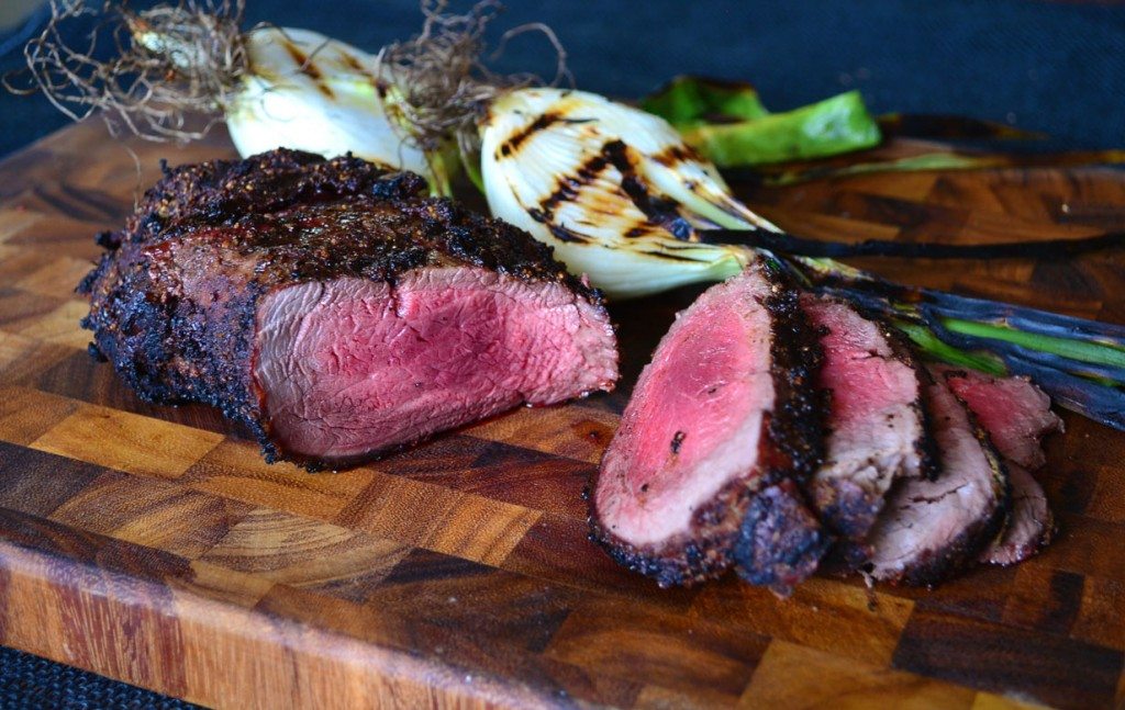 Sliced grilled beef tenderloin on a wooden cutting board