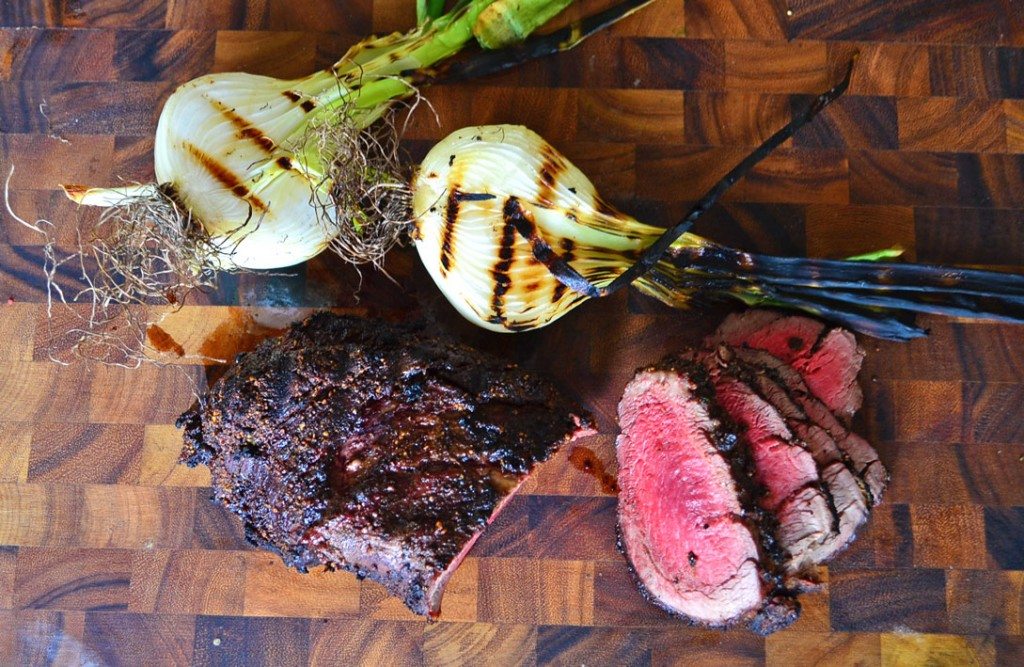 overhead shot of sliced beef tenderloin on a cutting board with onions