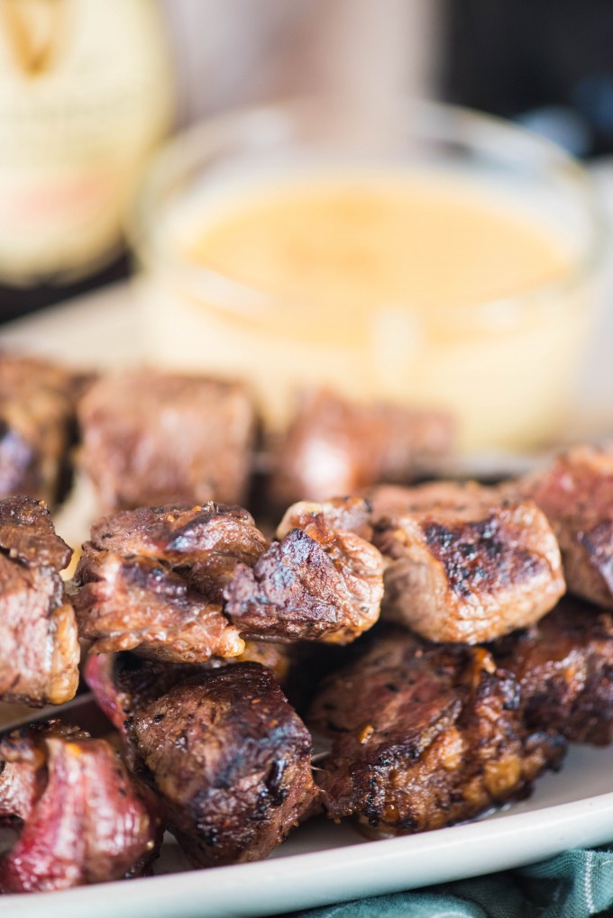 Guinness glazed steak skewers on white plate with gouda dipping sauce