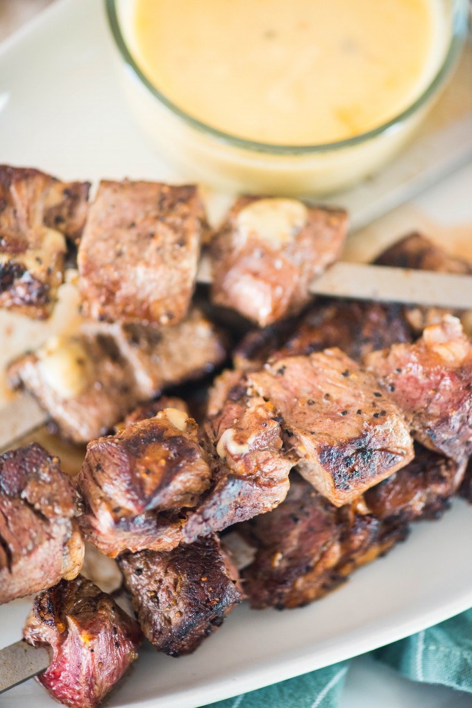 Guinness glazed steak skewers on white plate with gouda dipping sauce