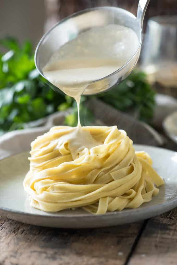 Ladle pouring alfredo sauce on a pile of fresh fettuccine