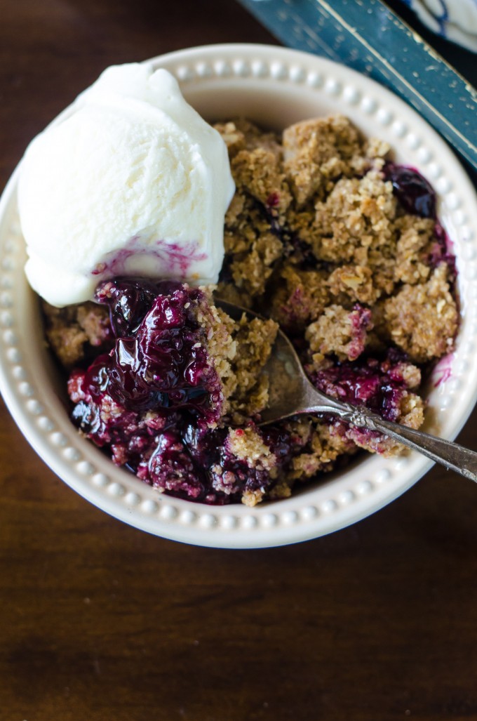 Blueberry crisp in a white bowl with vanilla ice cream