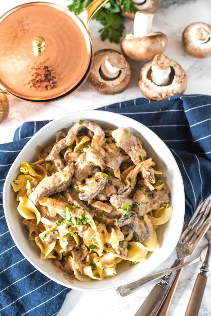 Beef Stroganoff over egg noodles in white bowl with blue napkin on marble surface