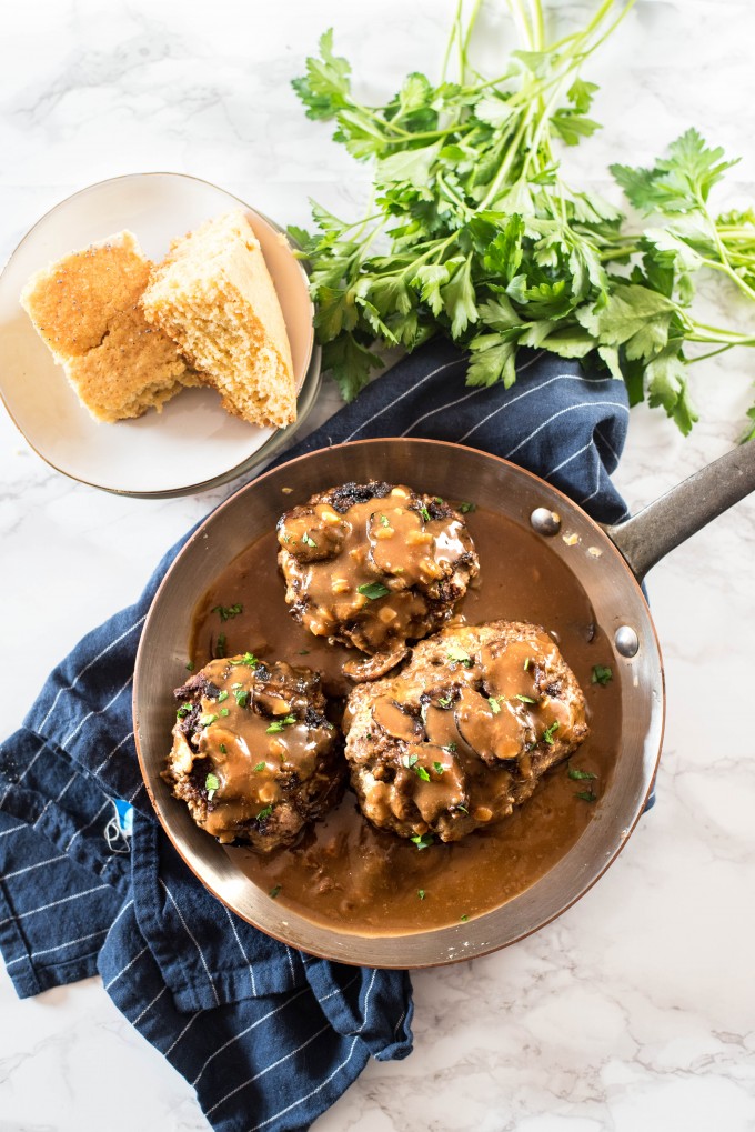 Salisbury steaks with mushroom gravy in a copper pan on a white marble surface with blue napkin