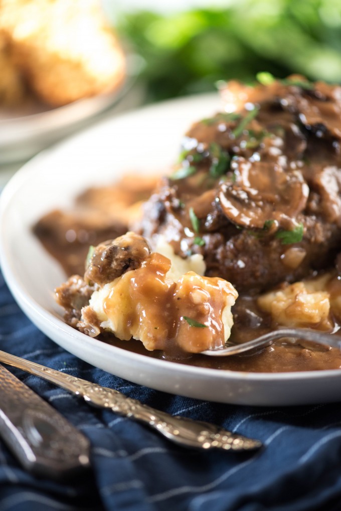 Bite of mashed potatoes on a fork on a plate of Salisbury steak 