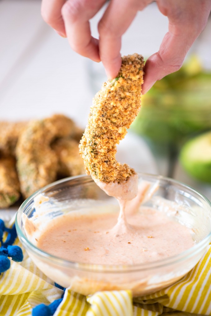 Breaded avocado fries dipped in sauce.