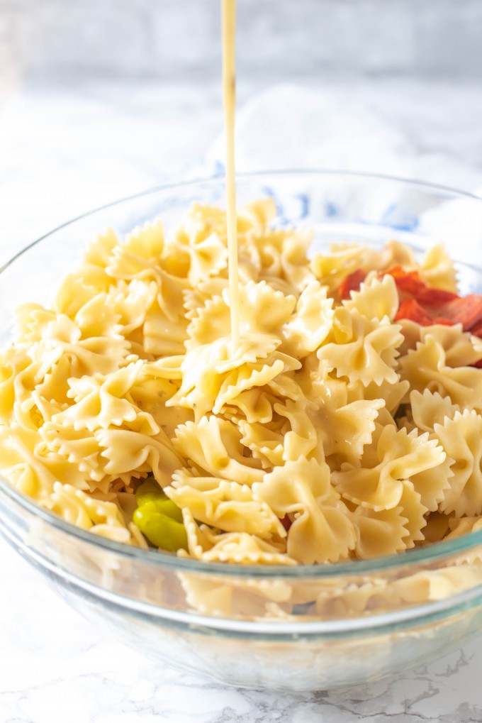 Italian dressing being poured onto a bowl of antipasto pasta salad