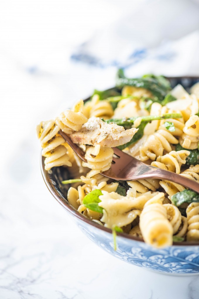 A fork in a blue bowl of pesto pasta salad