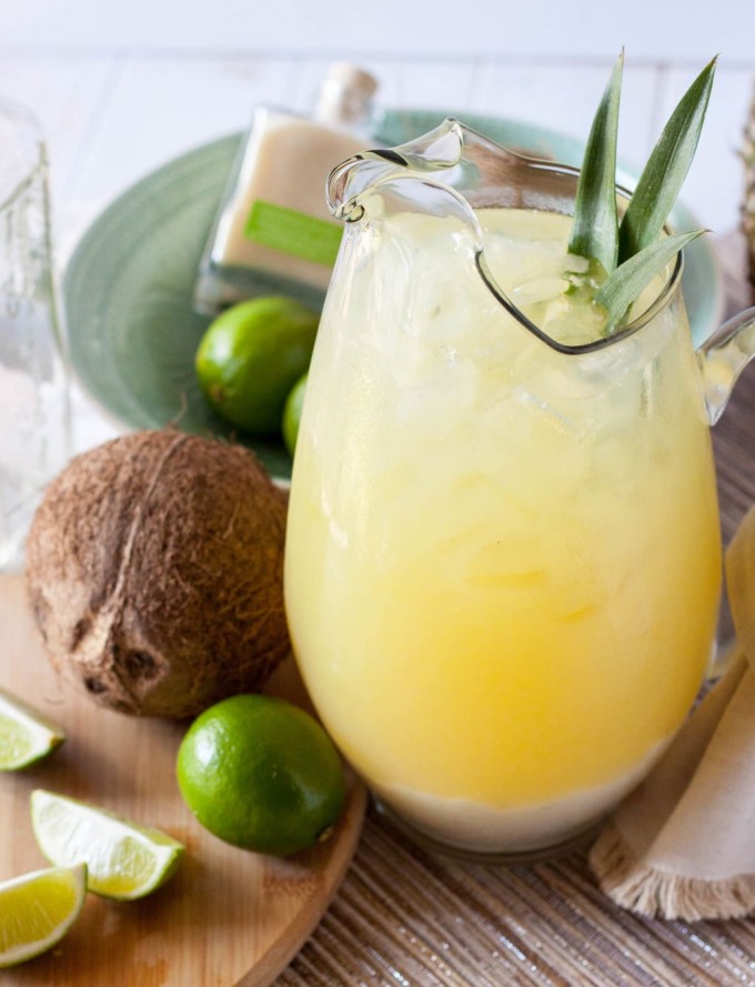 A pitcher of pineapple coconut margaritas with limes and a coconut