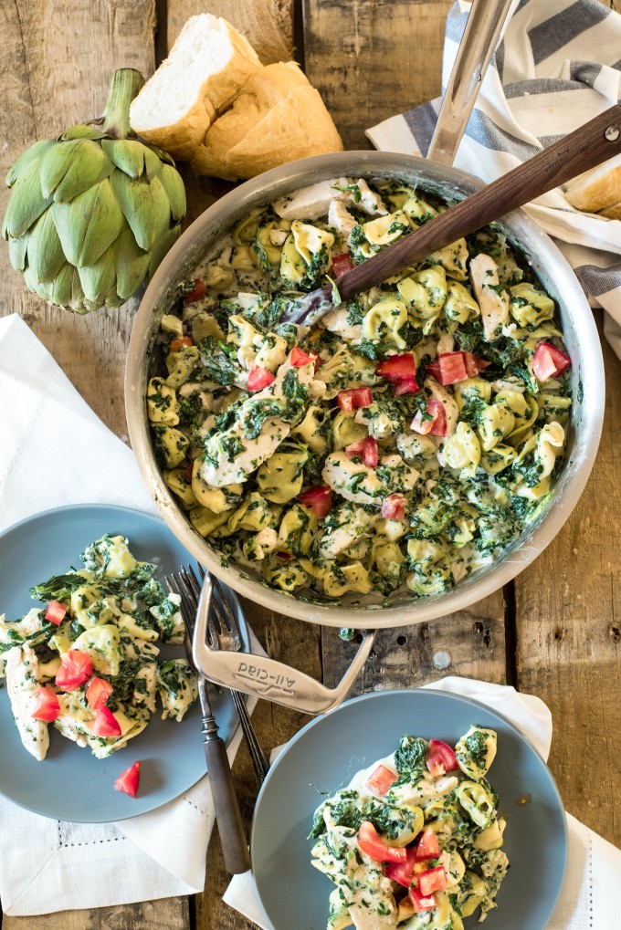 Spinach artichoke dip pasta in a pan with blue plates