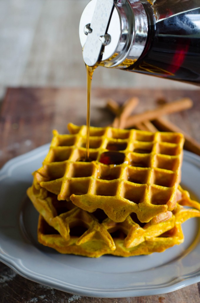 Stack of pumpkin waffles on a plate with maple syrup