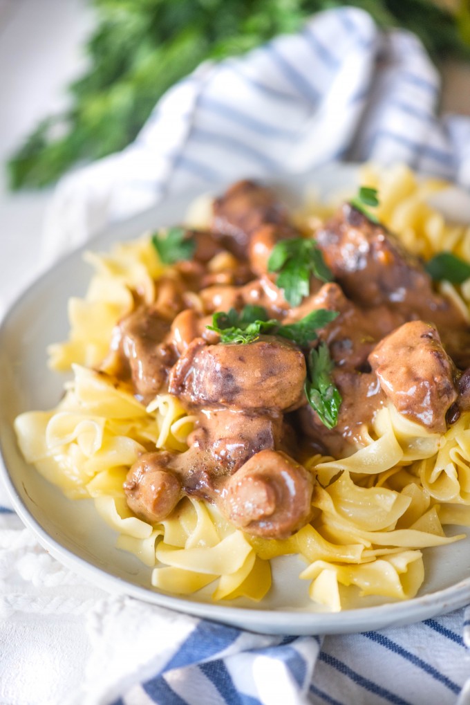 Instant pot beef tips over egg noodles on a white plate