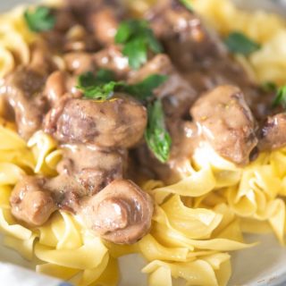 Close up of instant pot beef tips over egg noodles on a white plate