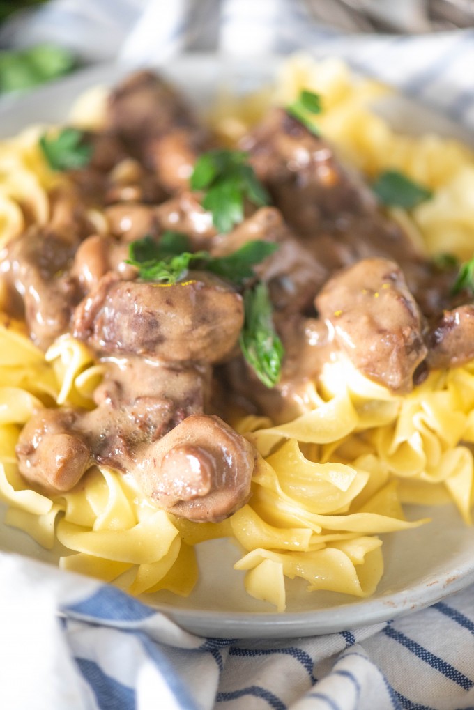 Close up of instant pot beef tips over egg noodles on a white plate