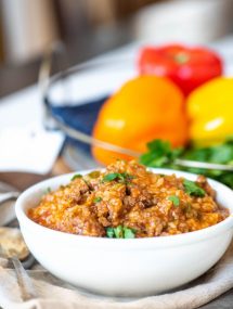 Stuffed pepper soup in a white bowl with peppers in the background