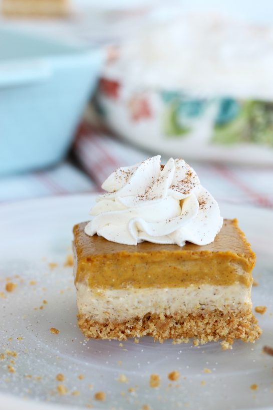 Slice of pumpkin cheesecake bars topped with whipped cream on a plate